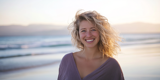 A woman stands at the beach at sunrise, she is smiling